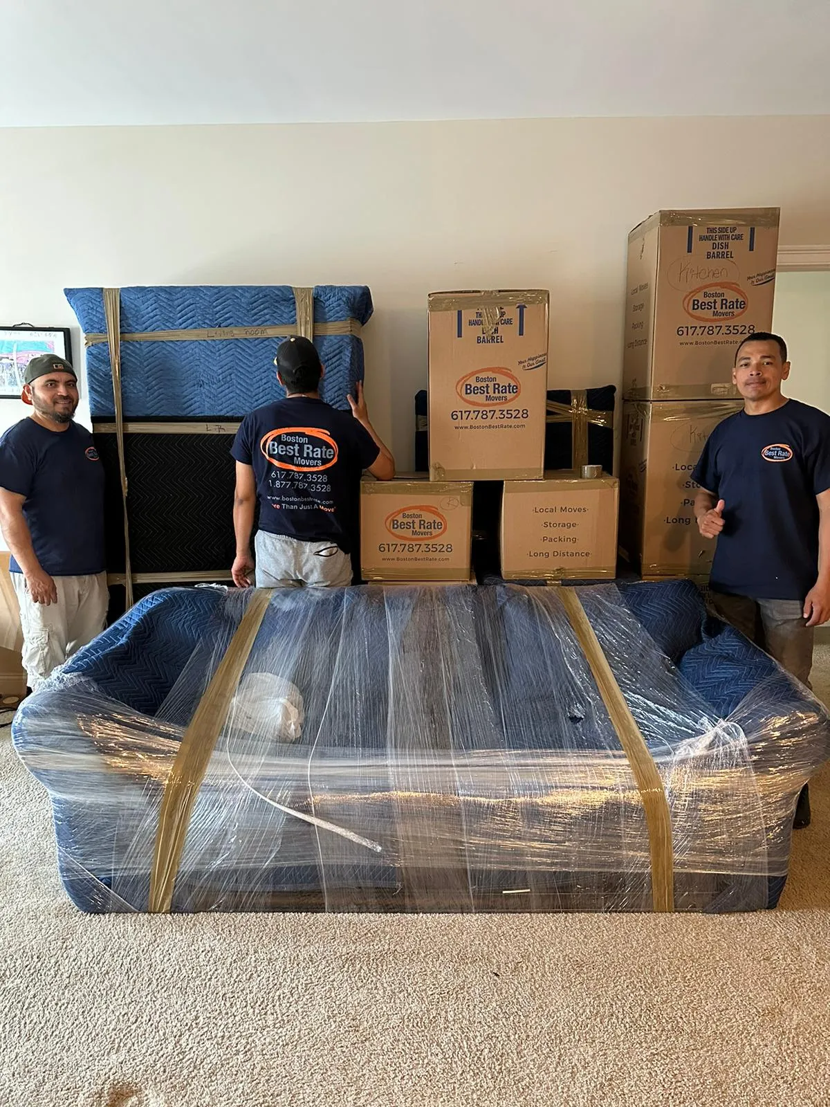 Three Boston Best Rate Movers crew members with packed furniture and branded boxes